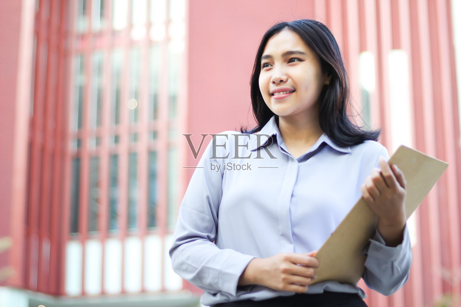 成功沉着的亚洲女商业顾问,穿着正装,拿着文件走过城市大楼,微笑的理财规划师自信地望向别处照片摄影图片