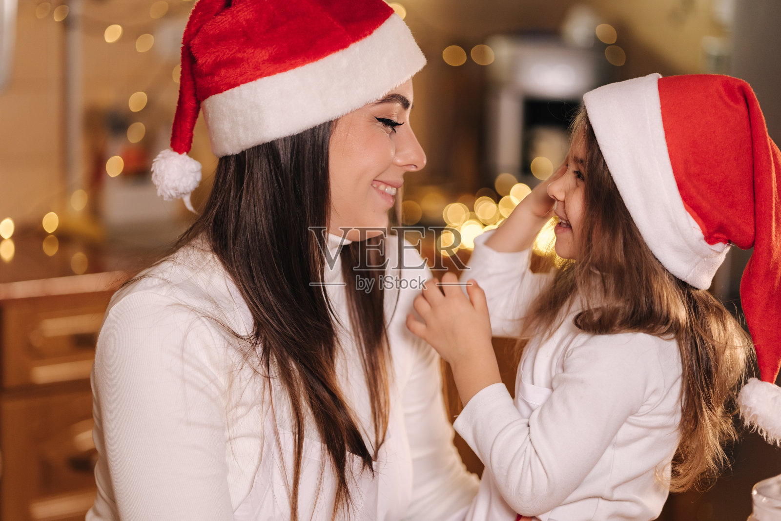 圣诞节期间可爱的小女儿和妈妈在厨房的照片。装饰适合餐桌上的树。女孩做姜饼照片摄影图片
