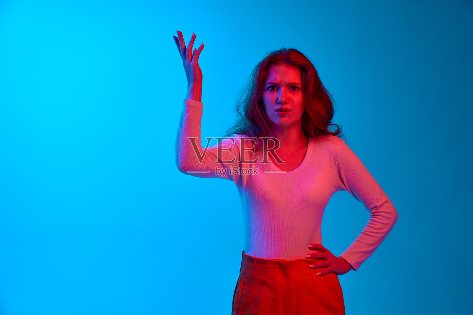 在霓虹灯的蓝色工作室背景下,年轻女子举手问询。误解照片摄影图片