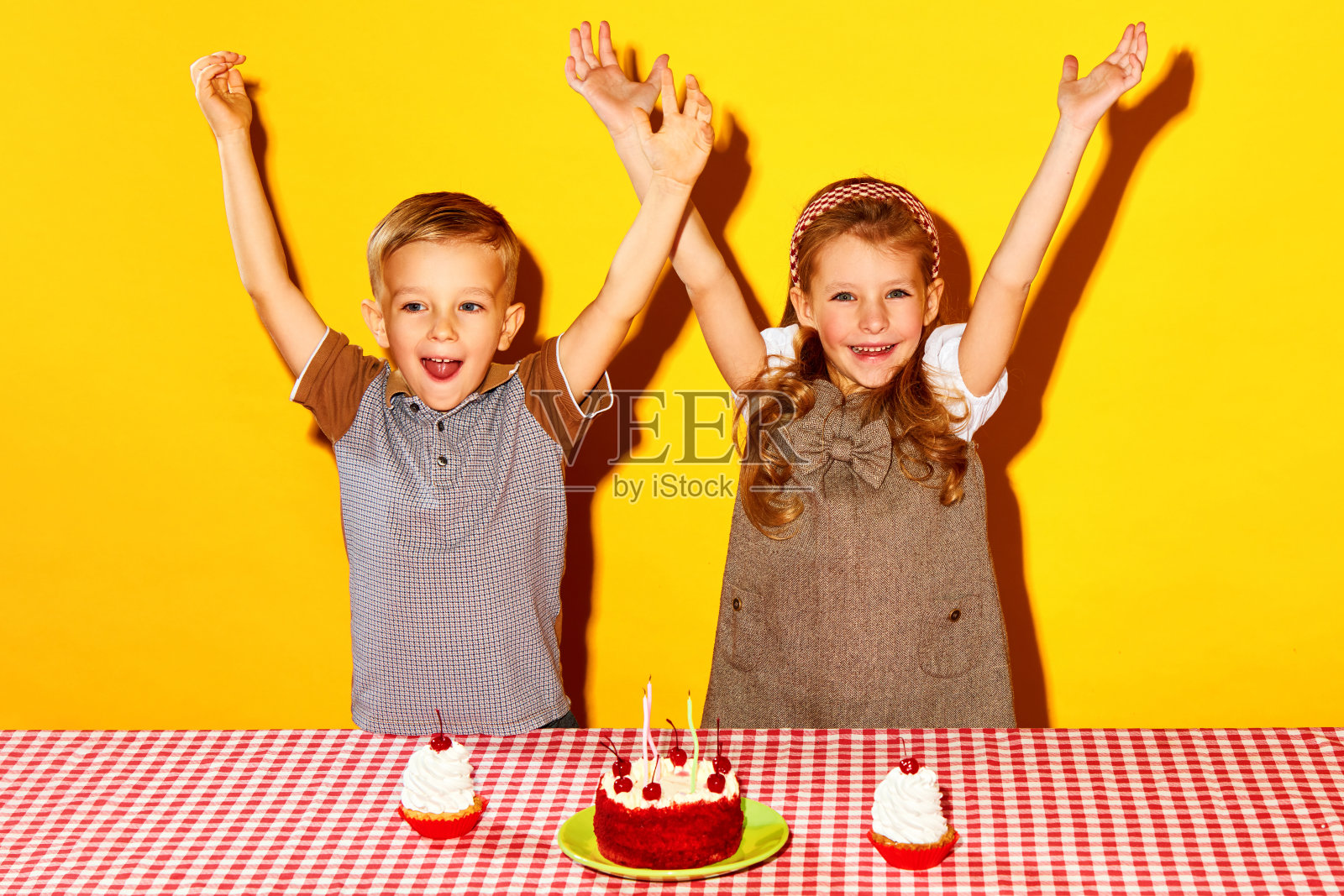 快乐,微笑,可爱的小男孩和女孩,孩子们,男孩和女孩站在桌子旁边,黄色背景的蛋糕照片摄影图片