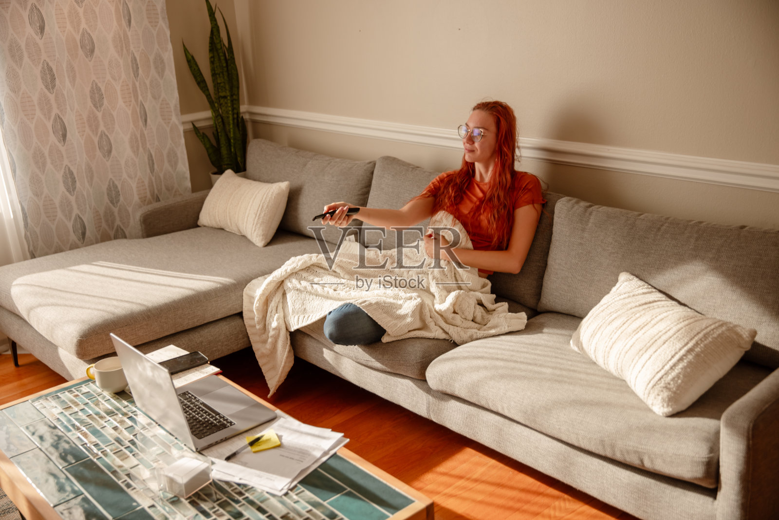 一个漂亮的年轻女孩,红头发,戴着眼镜,在家工作,一心多用。在休息时间看电视。照片摄影图片