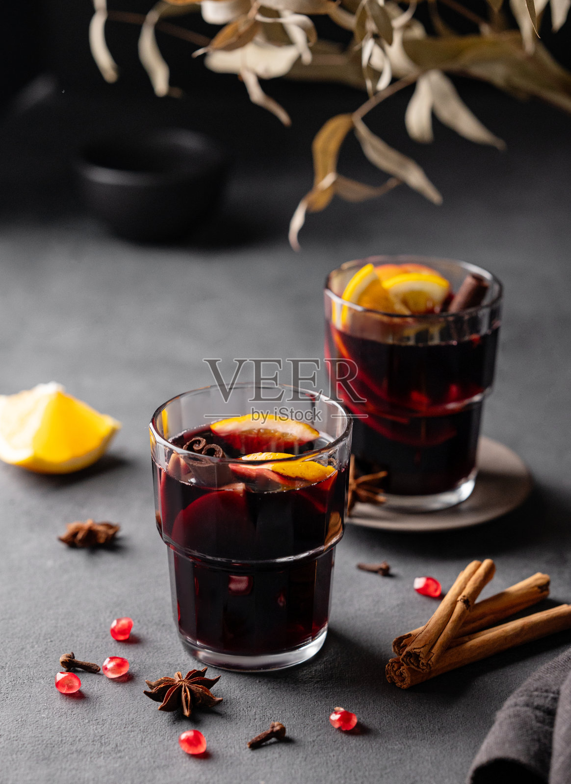 在深色背景下,用玻璃杯盛上带有橘子、苹果、石榴和肉桂的热葡萄酒。传统冬季热饮的概念,加入香料和水果照片摄影图片