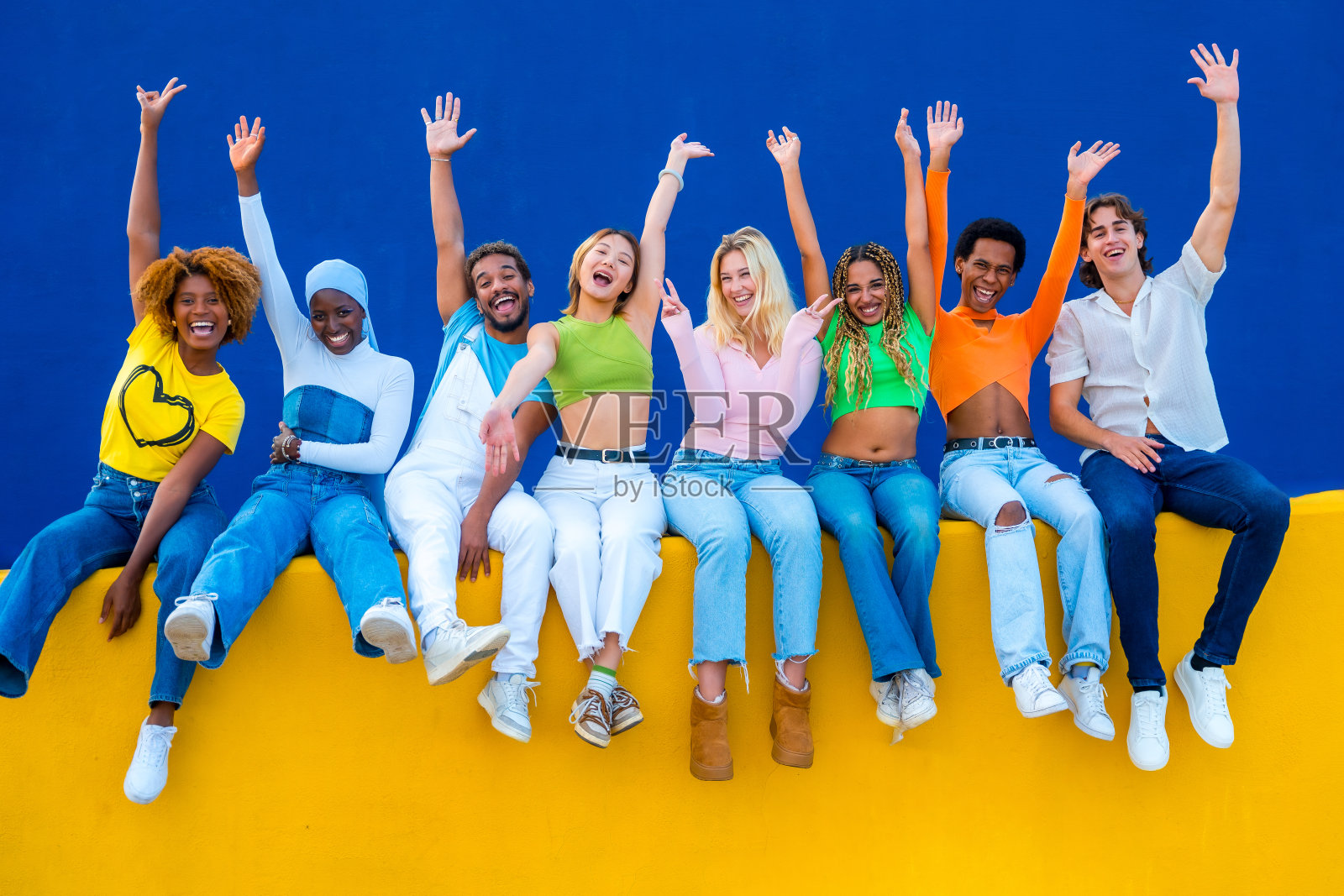 多民族朋友坐在墙上举手大笑照片摄影图片