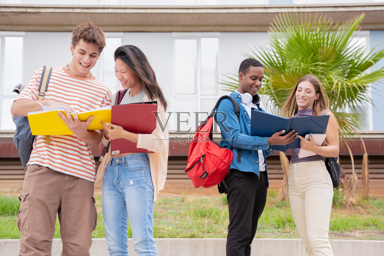 由四个快乐的十几岁的学生组成的多种族小组讨论着大学笔记。照片摄影图片