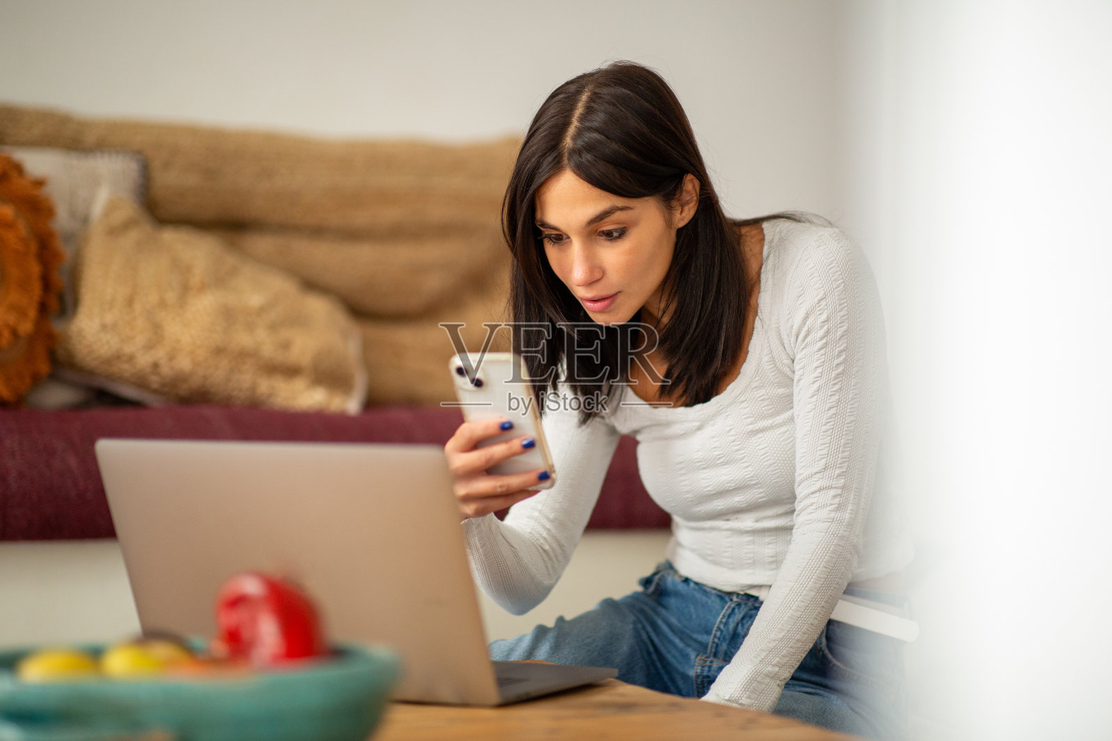 女人坐在家里拿着笔记本电脑和手机照片摄影图片