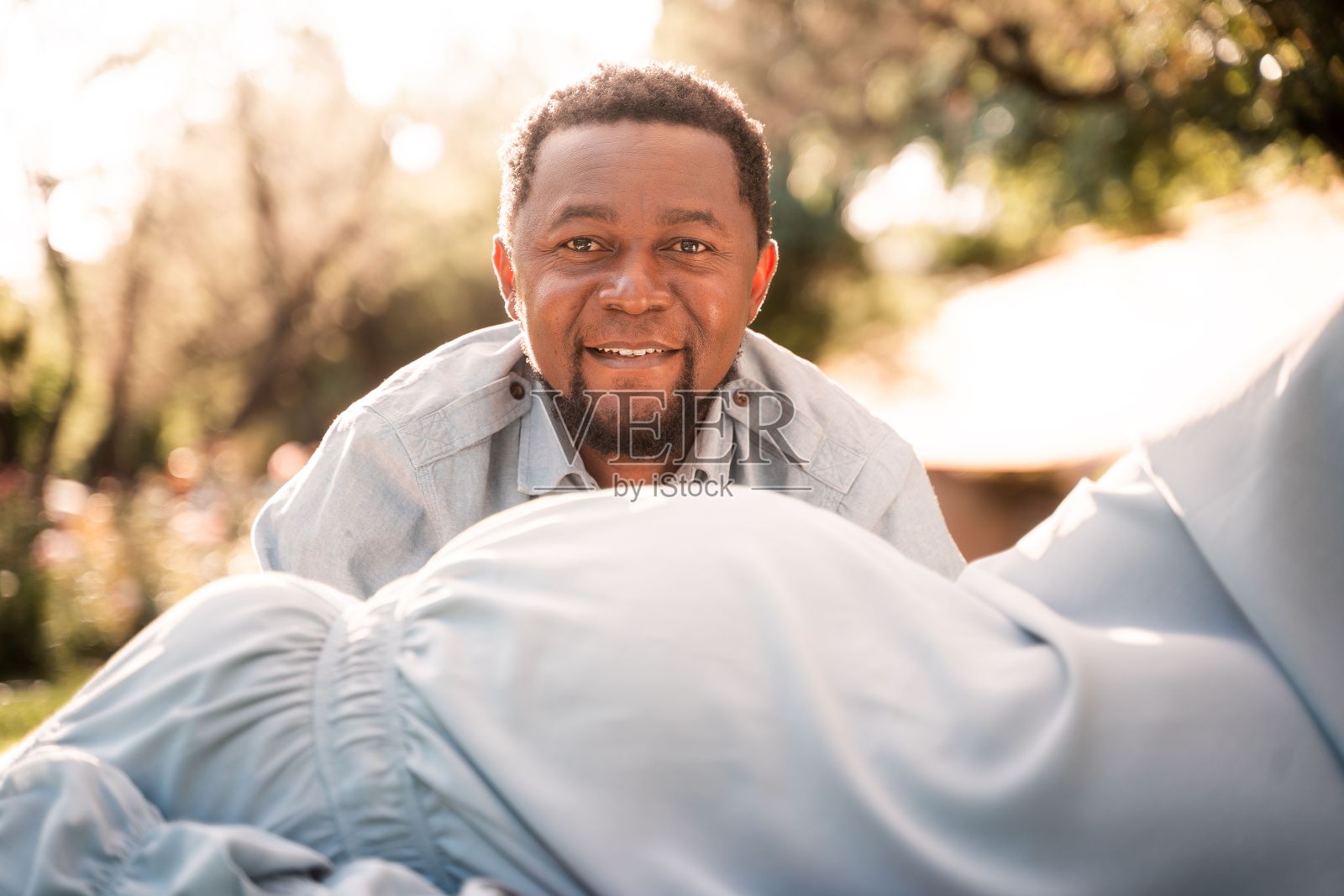 在阳光明媚的公园里,一名非洲男子从一名妇女怀孕的肚子后面偷看照片摄影图片