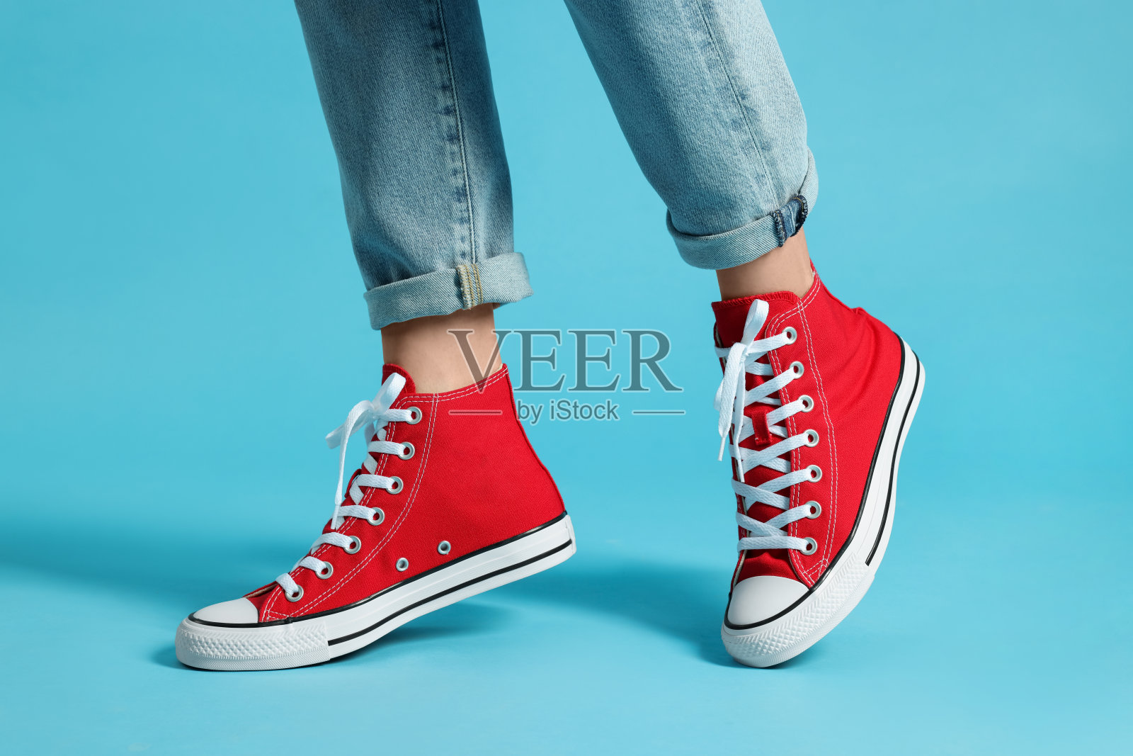 女人穿着时尚的胶鞋,浅蓝色背景,特写照片摄影图片