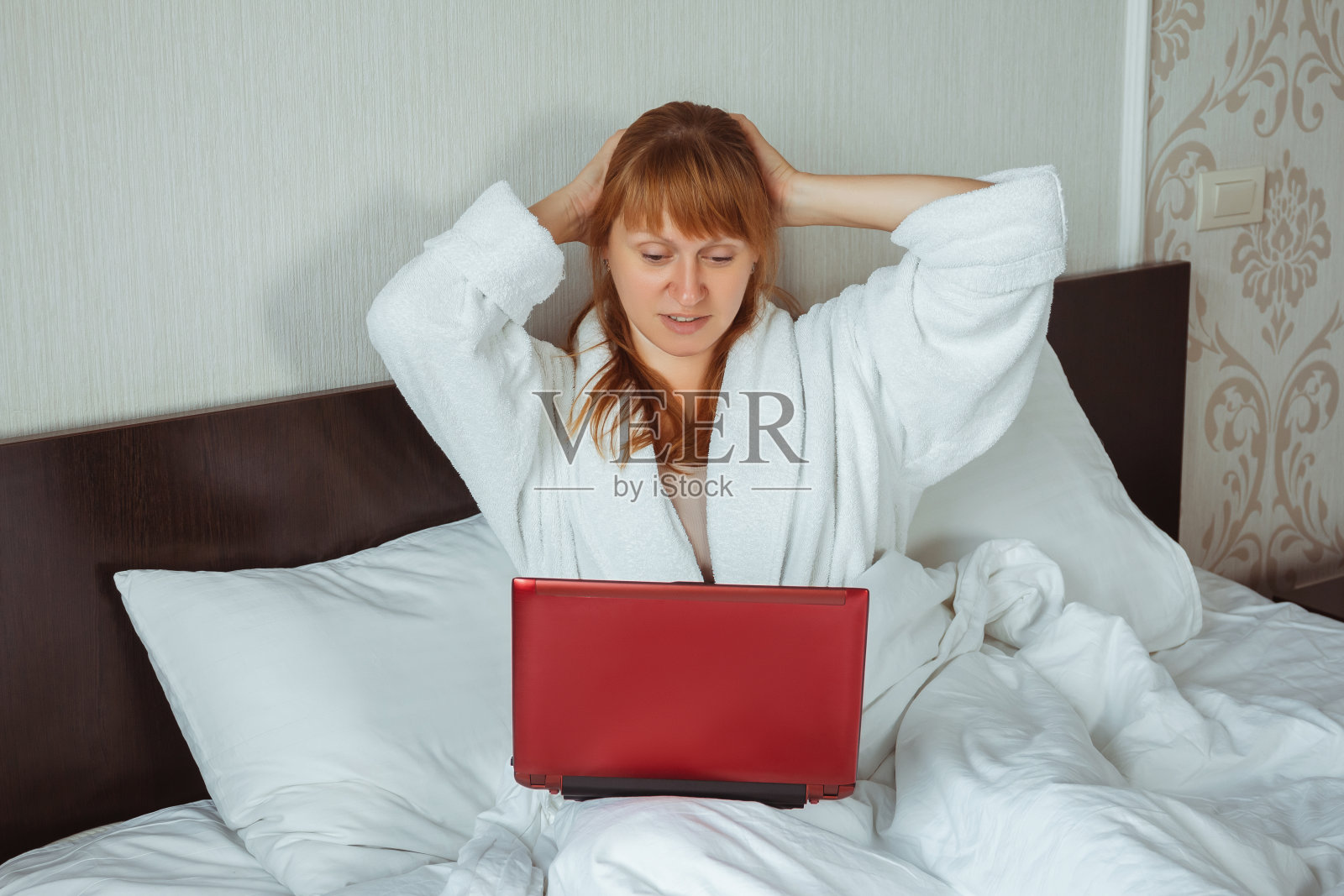 一个身穿白袍的女人坐在床上,惊恐地看着笔记本电脑的屏幕照片摄影图片