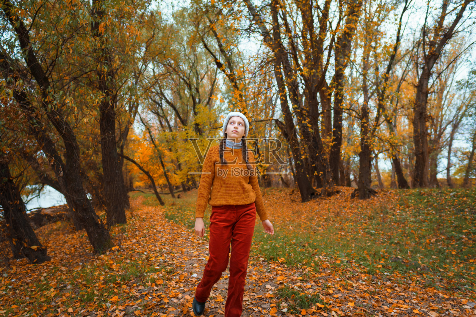 一个十几岁的小女孩走过秋天的森林,走过一片林间空地,欣赏着美丽的大自然和嫩黄的树叶照片摄影图片