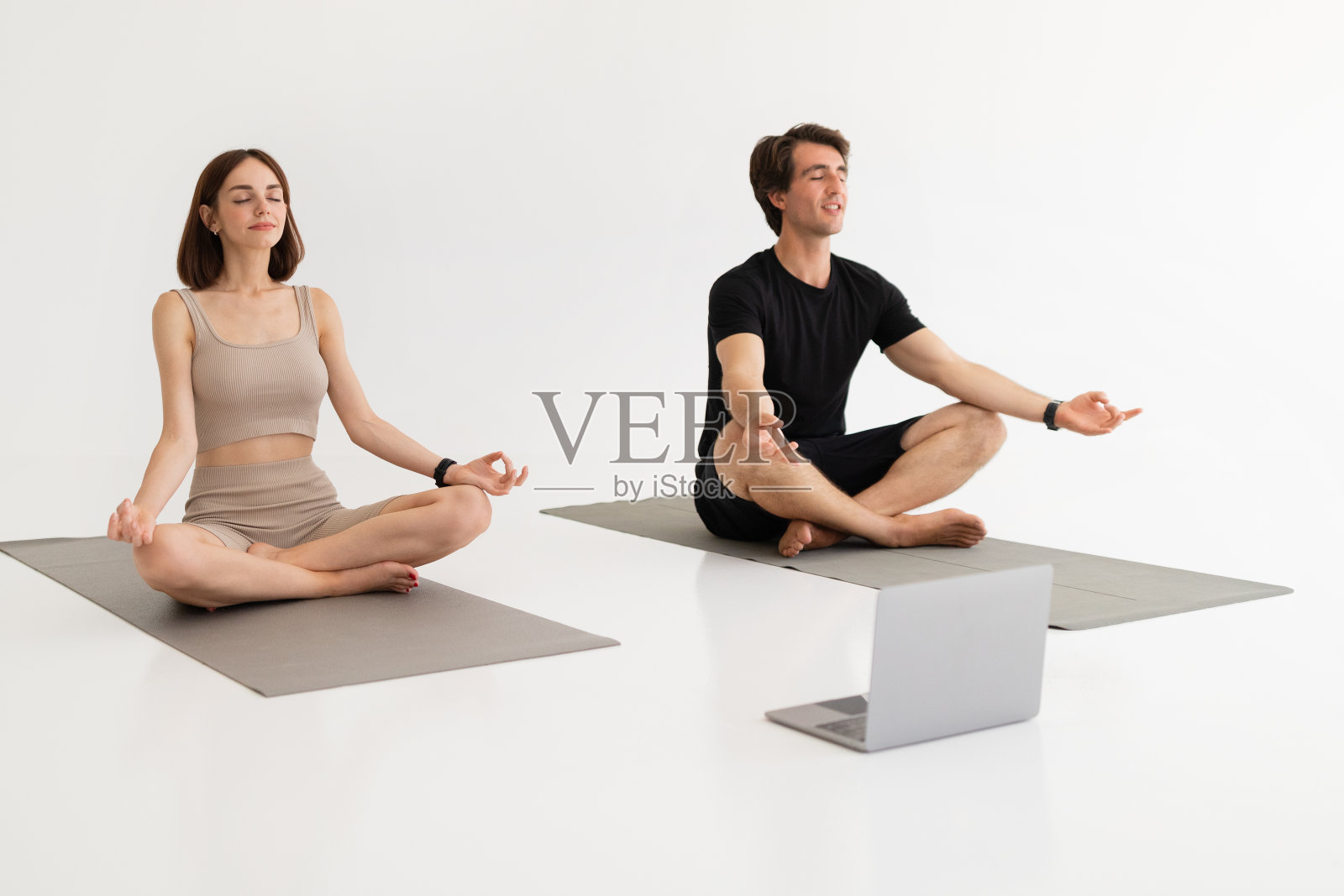 积极冷静的千禧一代白人夫妇穿着运动服训练,用笔记本电脑在莲花位练习瑜伽照片摄影图片