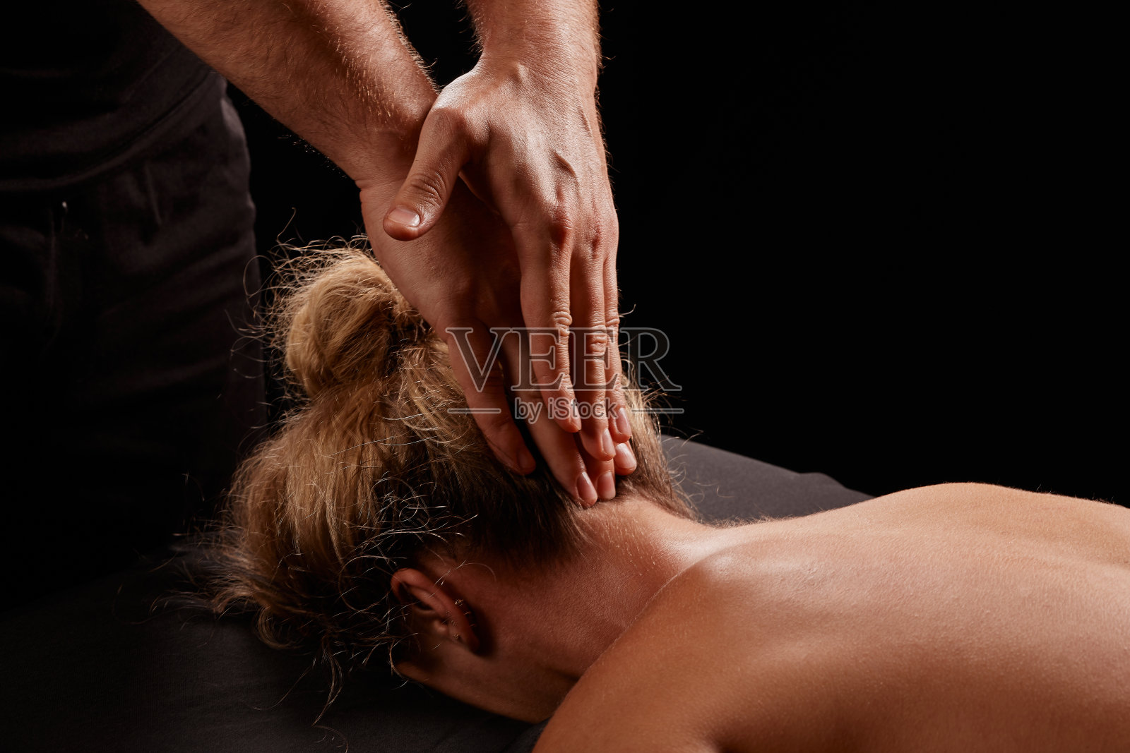 一个男按摩师在黑色背景上按摩一个女孩的脖子,颈部按摩照片摄影图片