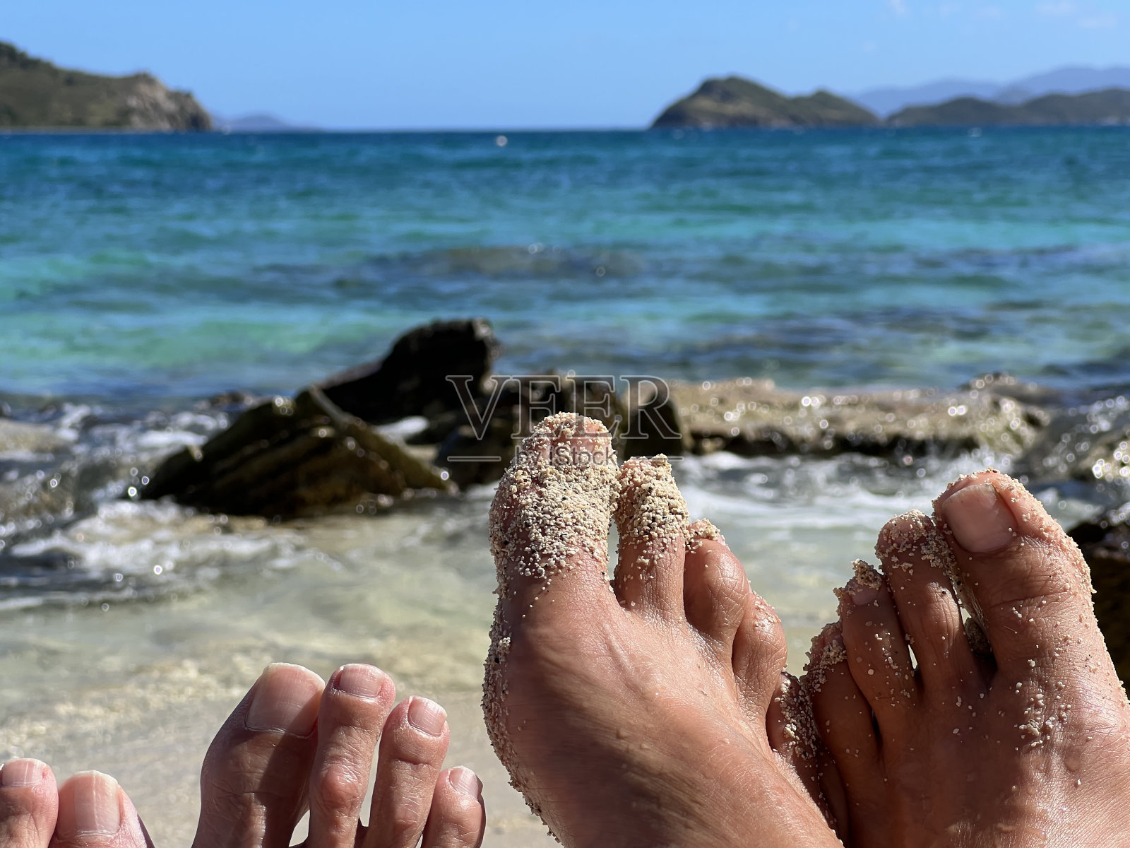 在圣托马斯岛上,一对夫妇的脚在加勒比海的水和岛屿的前景照片摄影图片