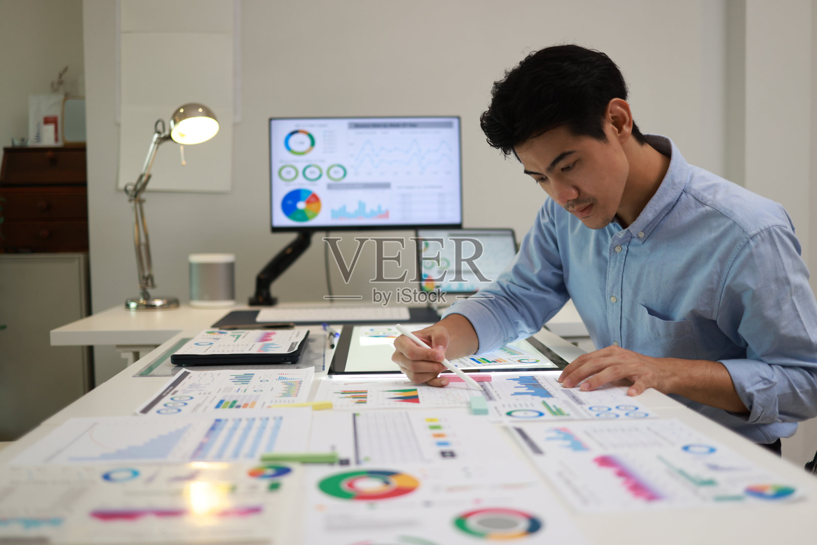 专注的商人在桌面显示器上分析市场报告,审阅纸质图表、财务统计和启动项目信息图表。照片摄影图片