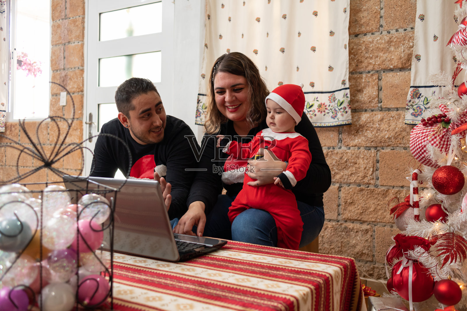 西班牙裔家庭在圣诞节进行视频通话,一对夫妇带着一个蹒跚学步的婴儿用笔记本电脑照片摄影图片