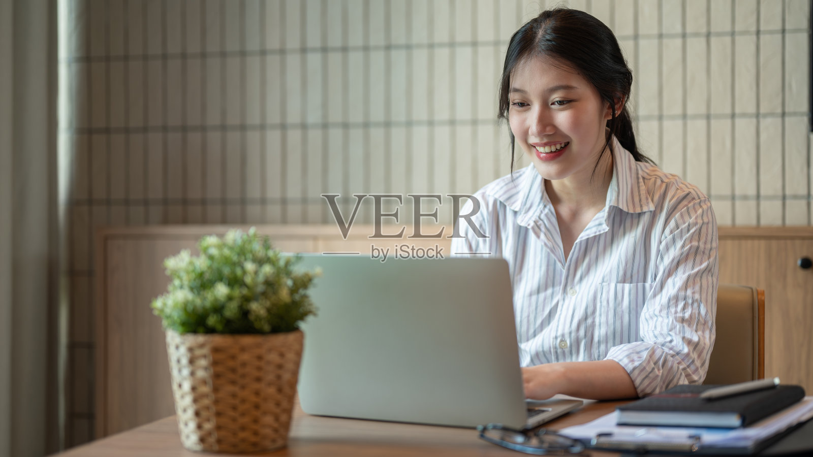 一位满意的亚洲女商人在一间现代化的办公室里用笔记本电脑做着她的项目。照片摄影图片