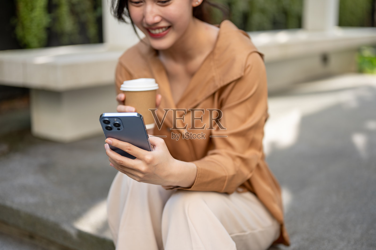 一个迷人的亚洲女人坐在室外的楼梯上,用她的智能手机。照片摄影图片