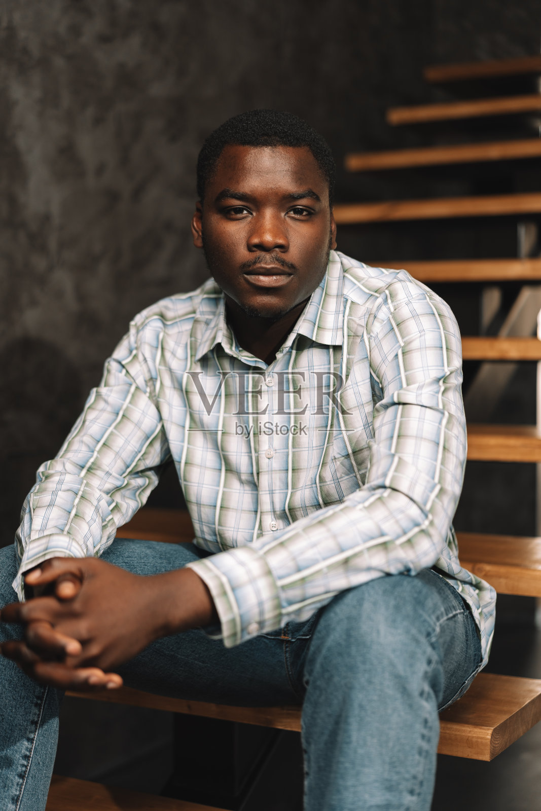 年轻的非洲男子坐在房间里的木梯上,肖像照片摄影图片