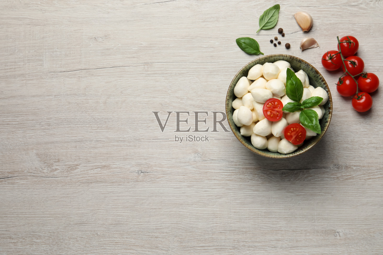 碗里放着美味的马苏里拉奶酪球,白色的木桌上放着西红柿和大蒜。文本空间照片摄影图片