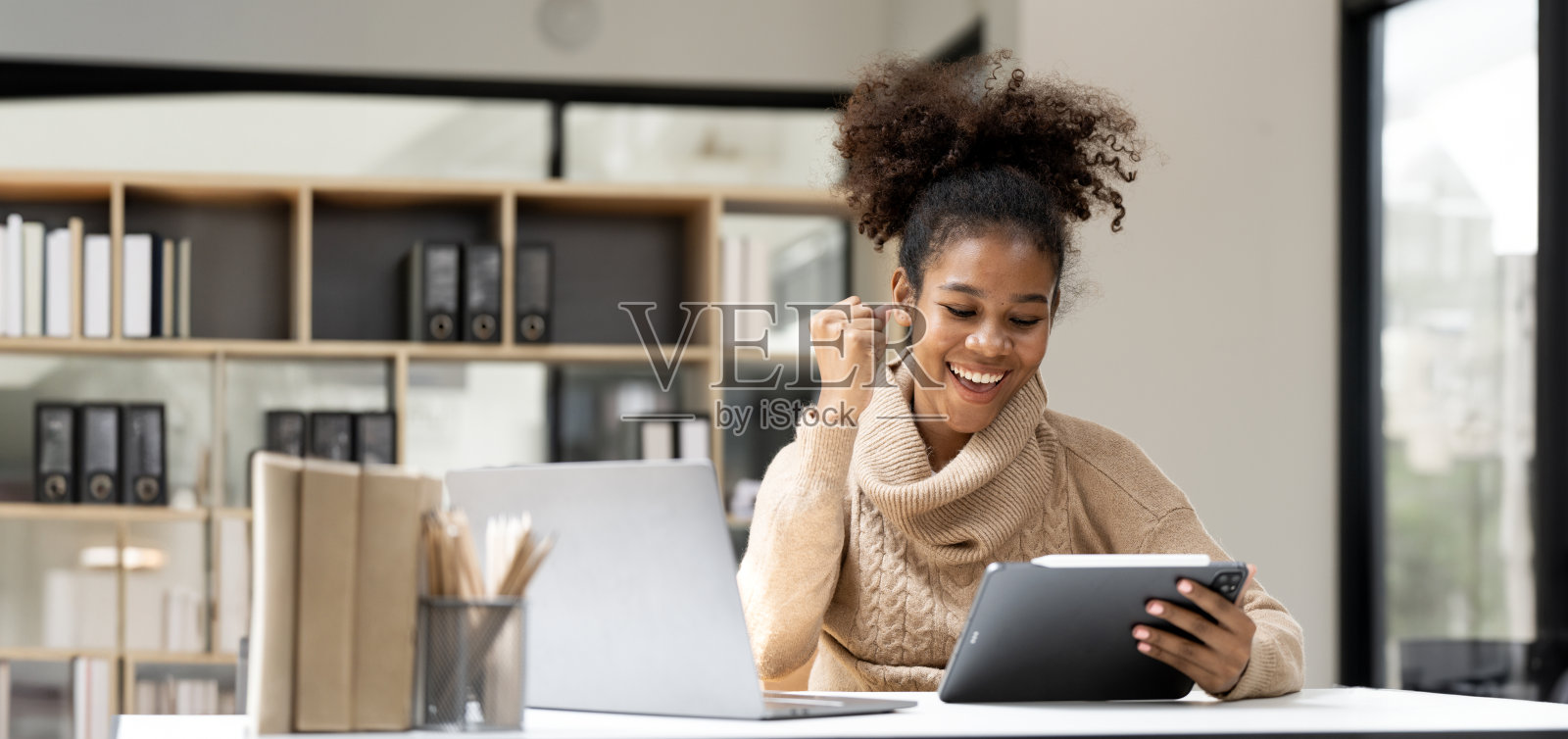 微笑的非洲黑人女商人一边使用平板电脑,一边在办公室用笔记本电脑工作。照片摄影图片