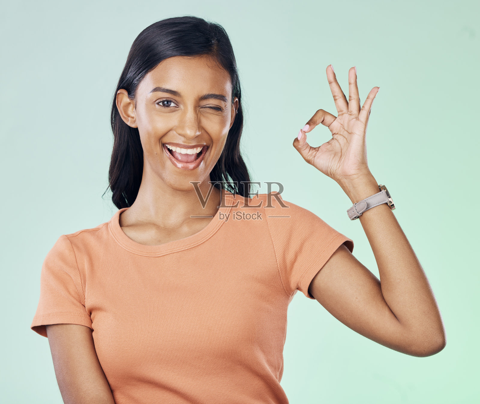 肖像,眨眼和女性在工作室完美的手势与积极,自信和快乐的心态。幸福、微笑和年轻的印度女性模特,她的手势被绿色背景隔离开来照片摄影图片