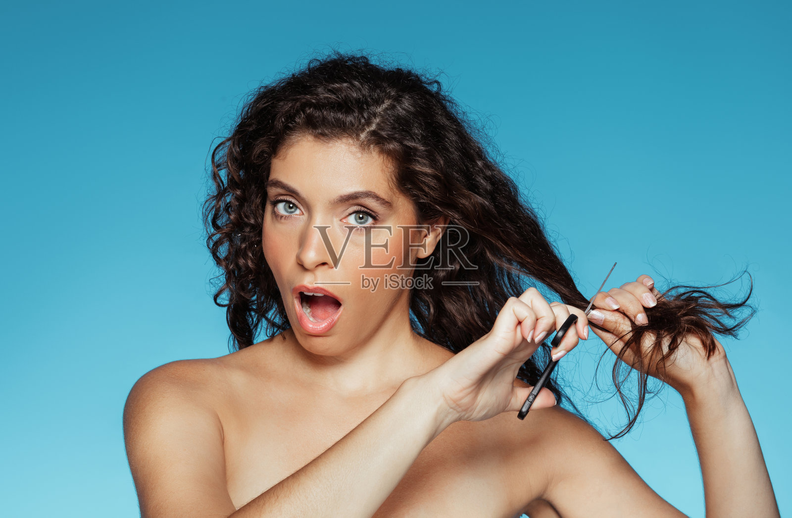 震惊的千禧年欧洲卷发女士张开嘴,用剪刀剪掉干燥的头发照片摄影图片