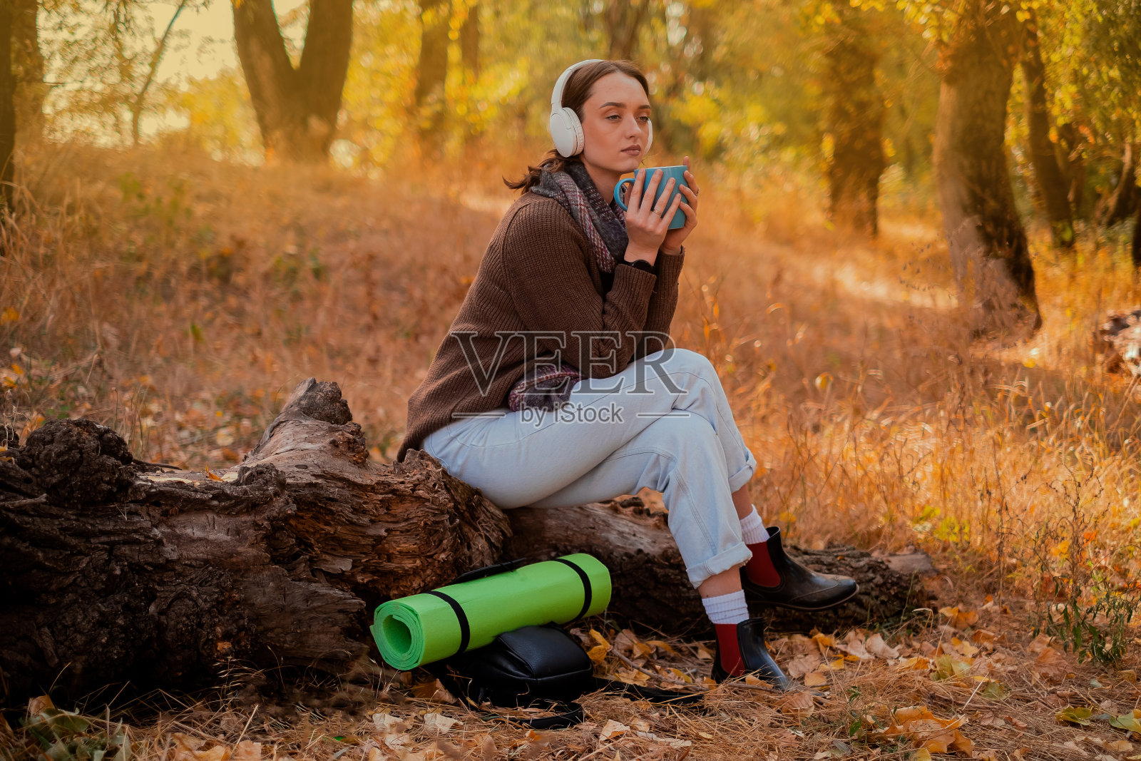 背着背包的女人用杯子喝茶,穿着棕色的毛衣,手里拿着地图,在秋天的森林里享受阳光明媚的天气,悬崖上的旅行者,徒步旅行照片摄影图片