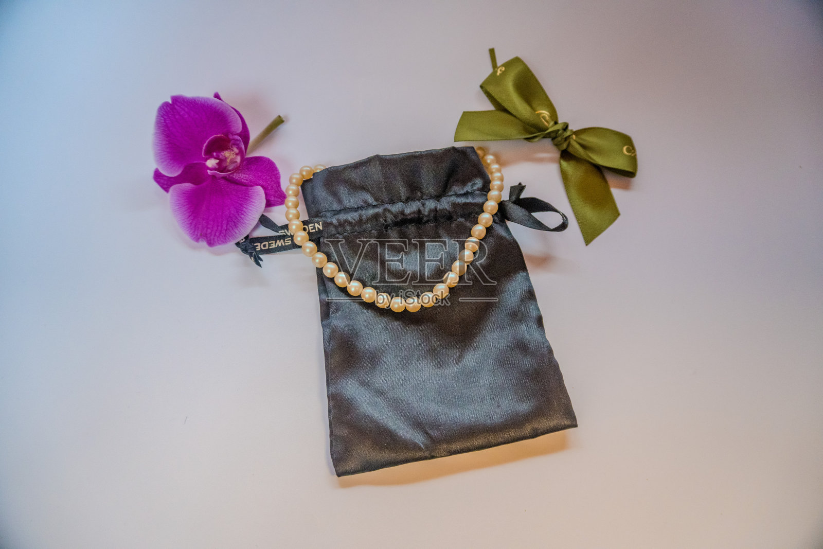 白色珍珠珠在黑色丝绸袋与紫色兰花在白色的背景照片摄影图片