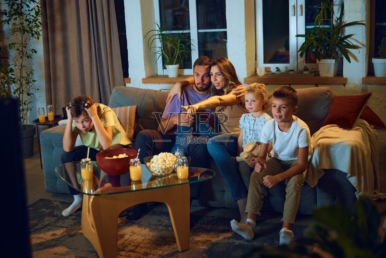 紧张的电影时刻。家人,父母和孩子坐在客厅的沙发上看电视。表达的情绪照片摄影图片