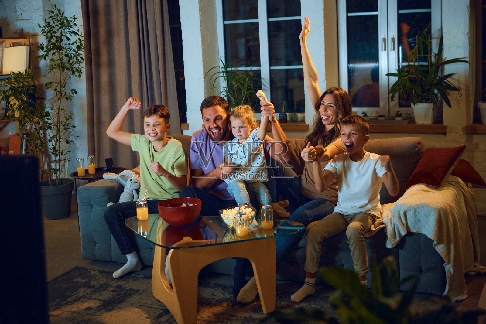 一家人在家里看足球比赛。妈妈,爸爸和孩子们坐在家里为运动队加油照片摄影图片