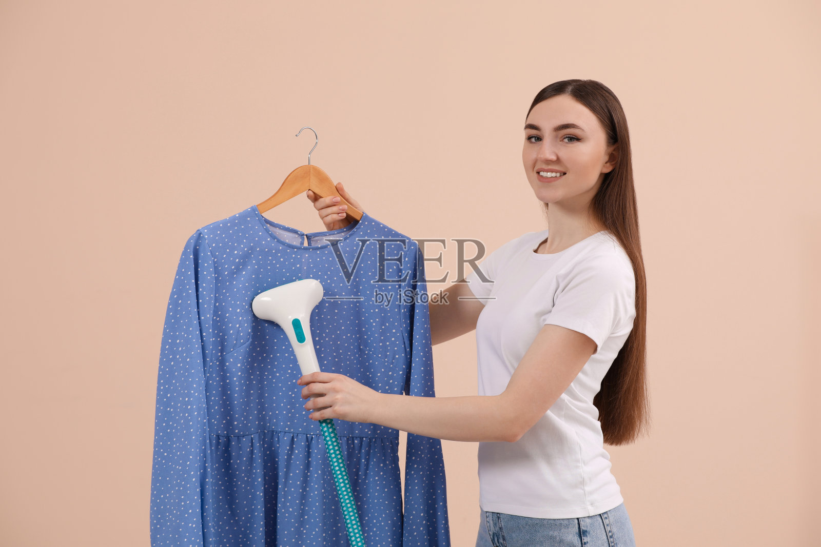 在米色背景下,挂在衣架上热气腾腾的女士衬衫照片摄影图片