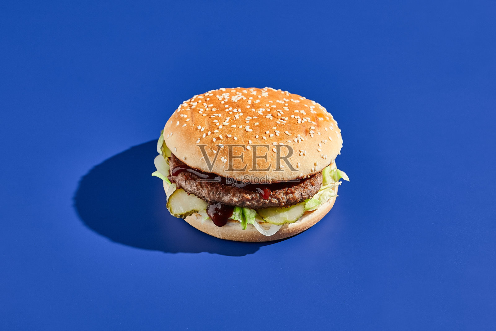 牛肉汉堡蓝色背景与硬阴影。美式垃圾食品的极简风格。汉堡时尚风格。简单的汉堡色背景。照片摄影图片