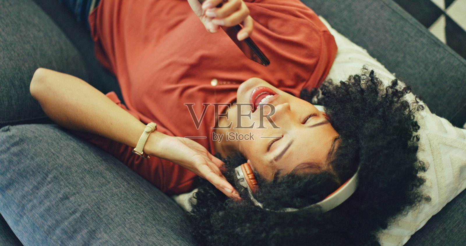 快乐的女人坐在沙发上,在客厅里听音乐,打电话和唱歌,用流媒体收音机放松。耳机,能量和女孩在家里的沙发上听音频与互联网,技术和自由。照片摄影图片