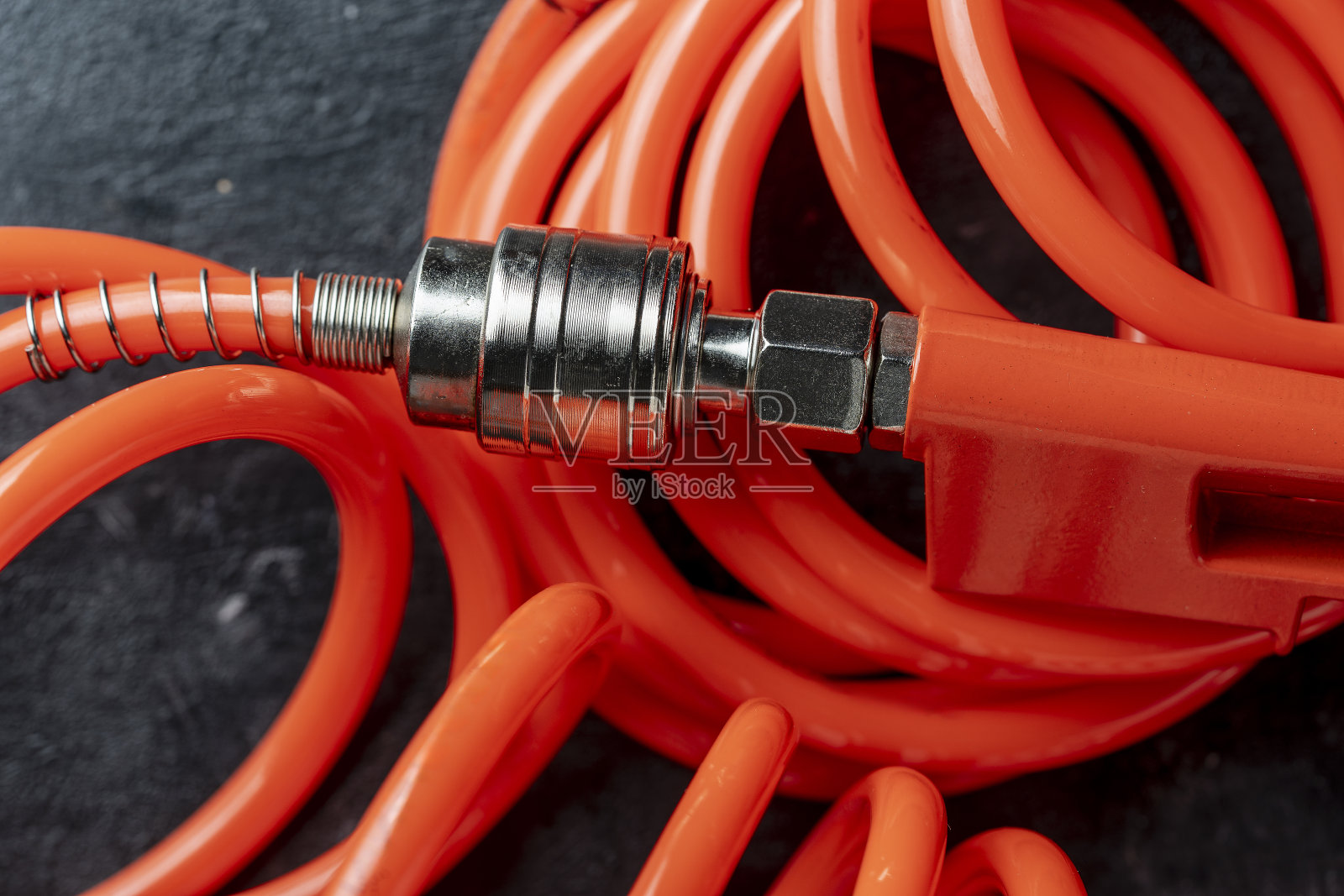 一个橙色的空气软管和一个黑色背景上的软管接头,特写。空气压缩机软管和手枪的详细说明照片摄影图片