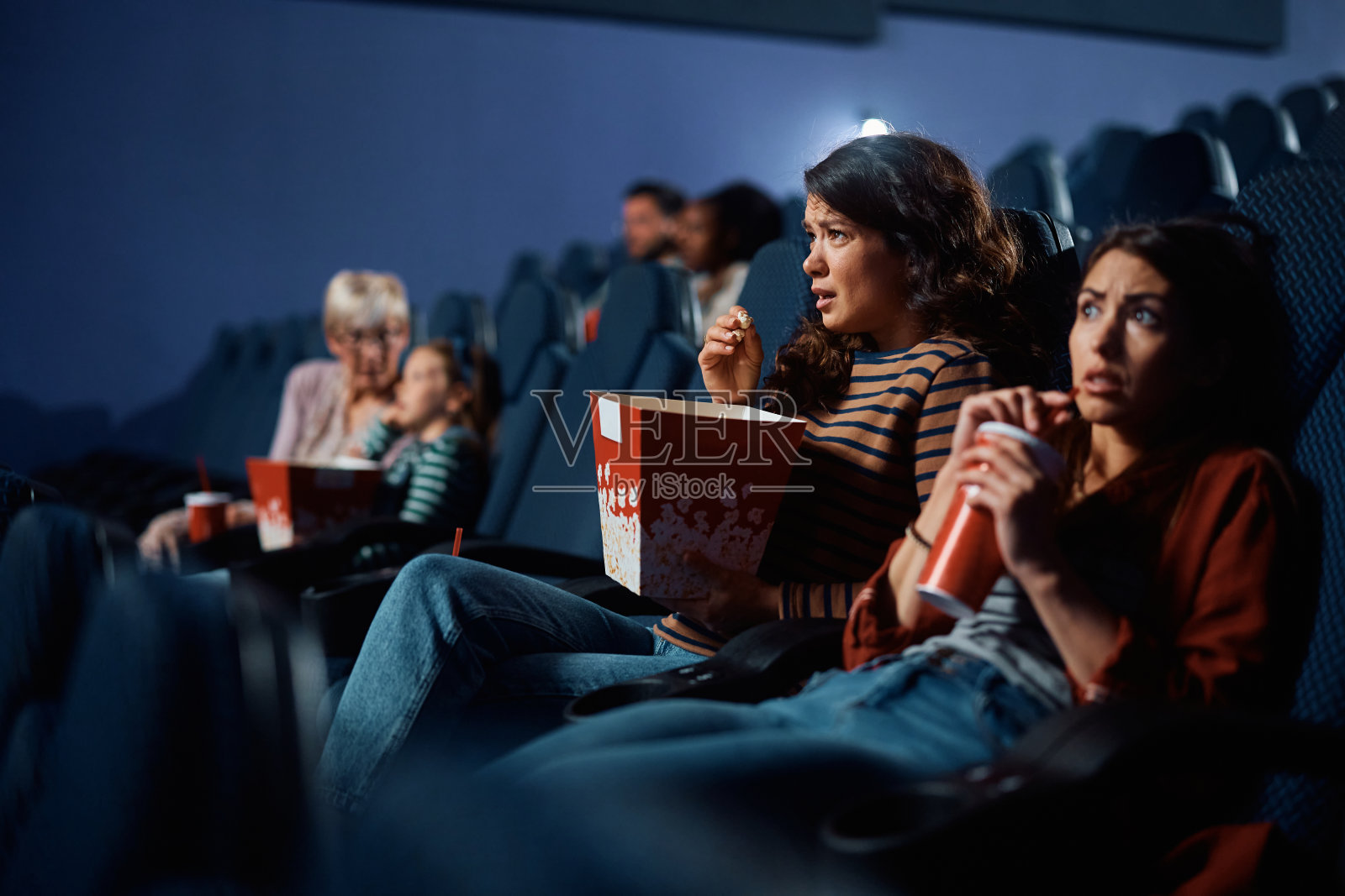 年轻女性在电影院看恐怖电影。照片摄影图片