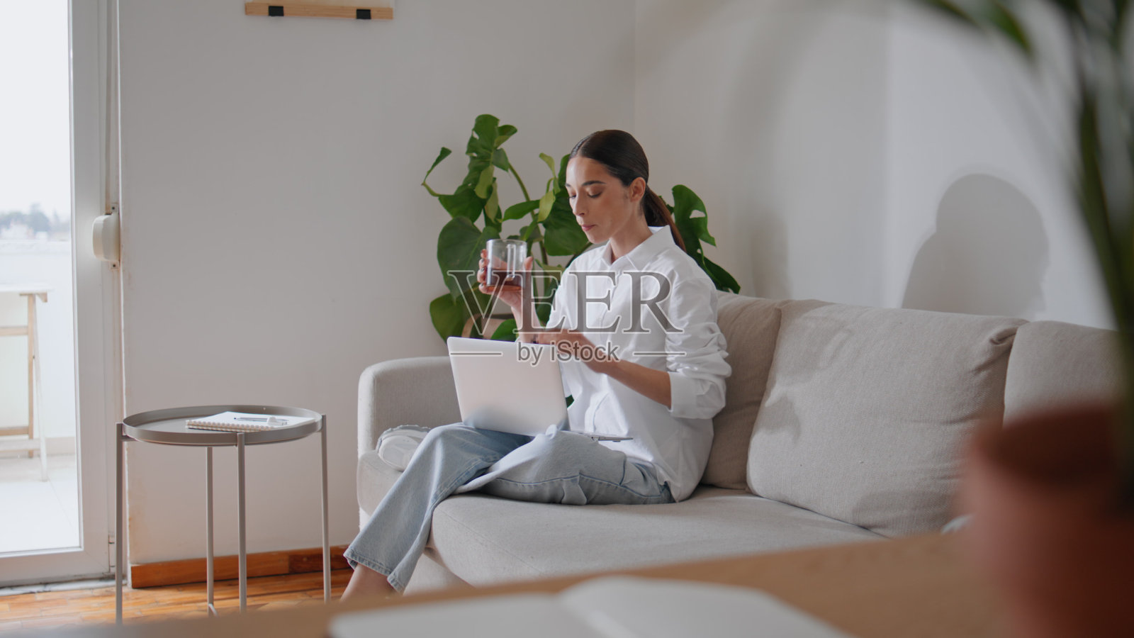 年轻女士在舒适的沙发上喝茶发短信玩电脑。女性工作笔记本电脑照片摄影图片