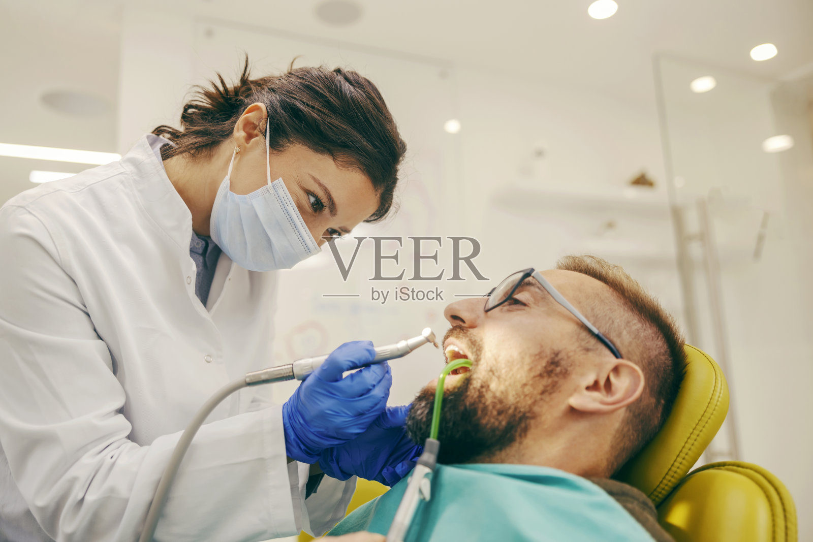 当病人坐在椅子上时,牙医正在钻有蛀牙的牙齿。照片摄影图片