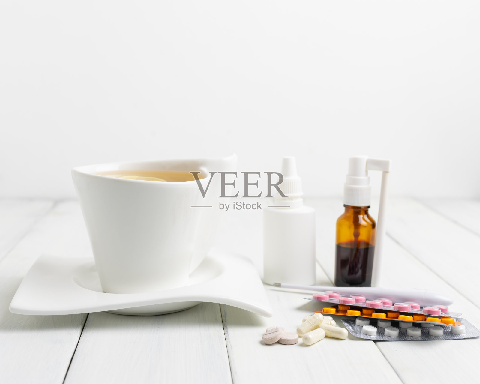 装着柠檬的茶杯,感冒药,药,温度计,胶囊和药片,用水泡包装放在木桌上。家庭治疗流感和冠状病毒的概念照片摄影图片