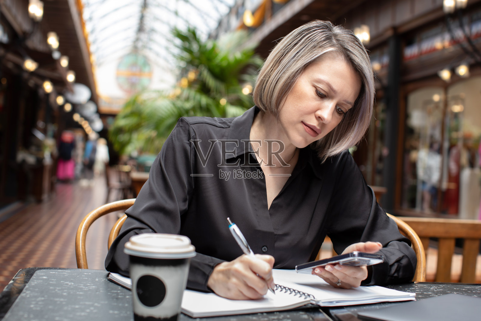 一位年轻的女商人坐在咖啡馆里,端着一杯咖啡,在日记本上做着笔记。照片摄影图片