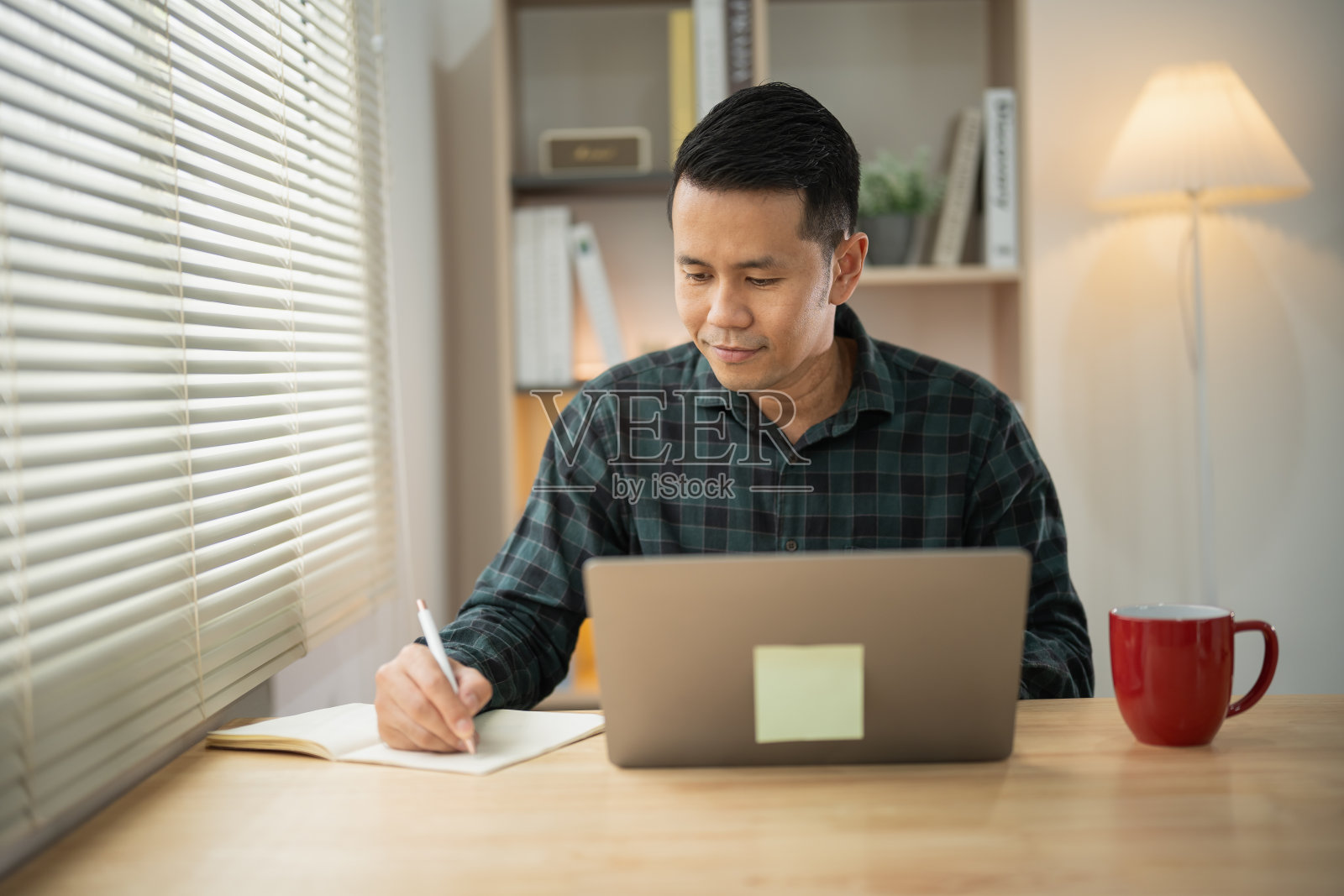 亚洲自由职业者快乐,放松,微笑,在家里用笔记本电脑打字,在笔记本上写笔记。企业家在客厅里为生意工作。商务在家工作的概念。照片摄影图片