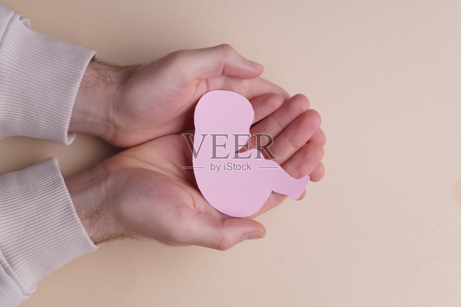 女性健康。男子抱着米色背景的新生纸人像,俯视图照片摄影图片