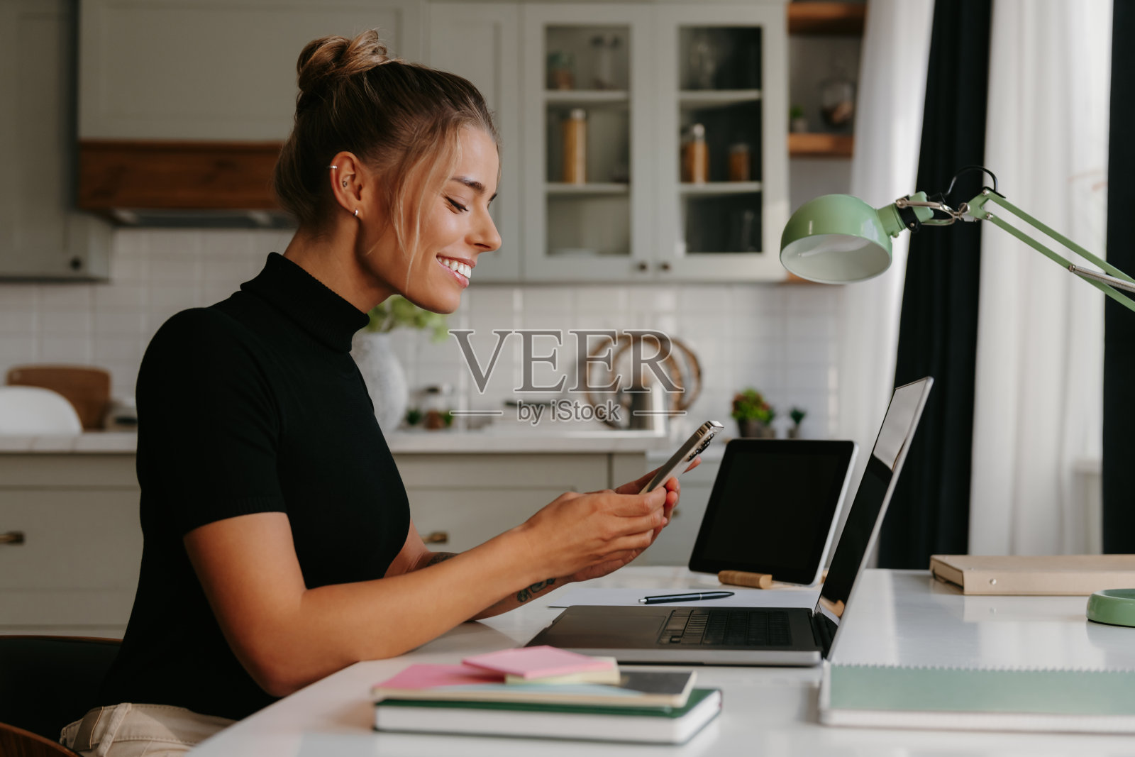 微笑的年轻女子坐在办公桌前,在家工作时使用智能手机照片摄影图片