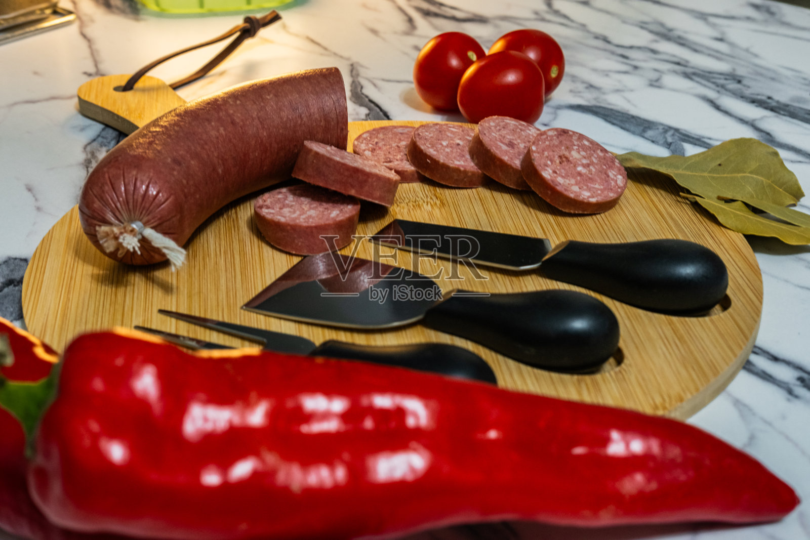 把Sucuk切成片放在一个木制的盘子里,周围点缀着红辣椒和西红柿照片摄影图片