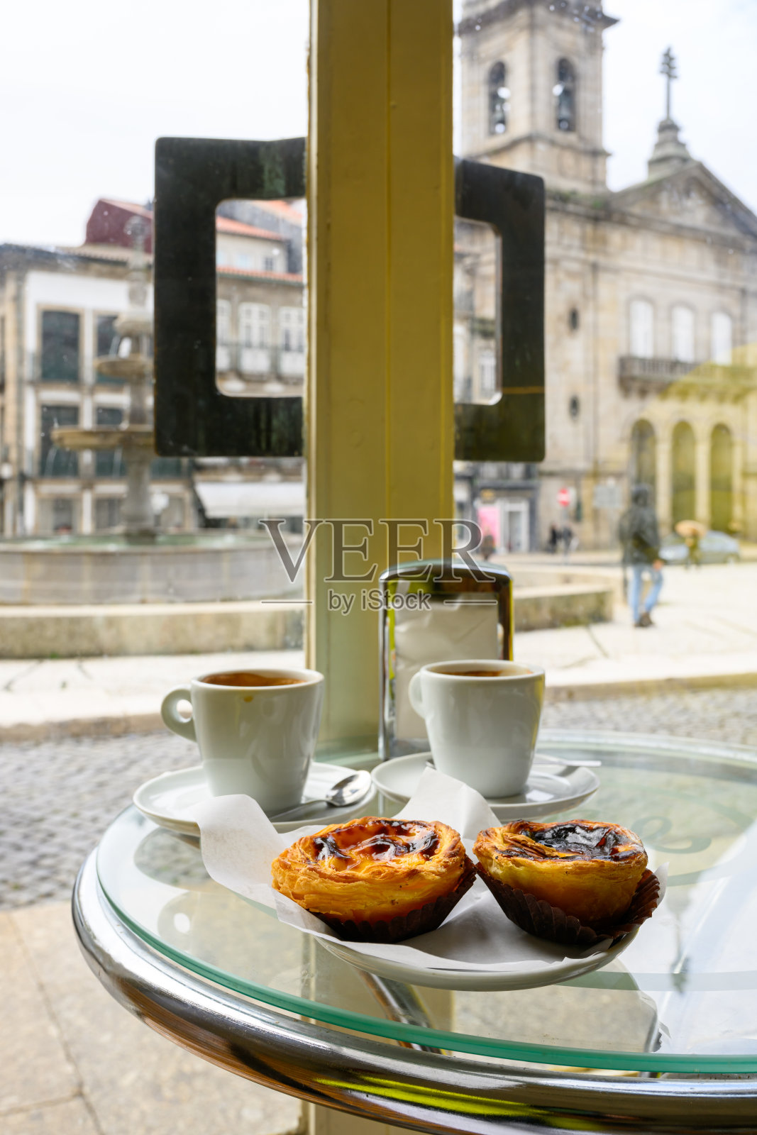 葡萄牙吉马良斯,面对老广场的玻璃桌上放着蛋挞和卡布奇诺咖啡照片摄影图片