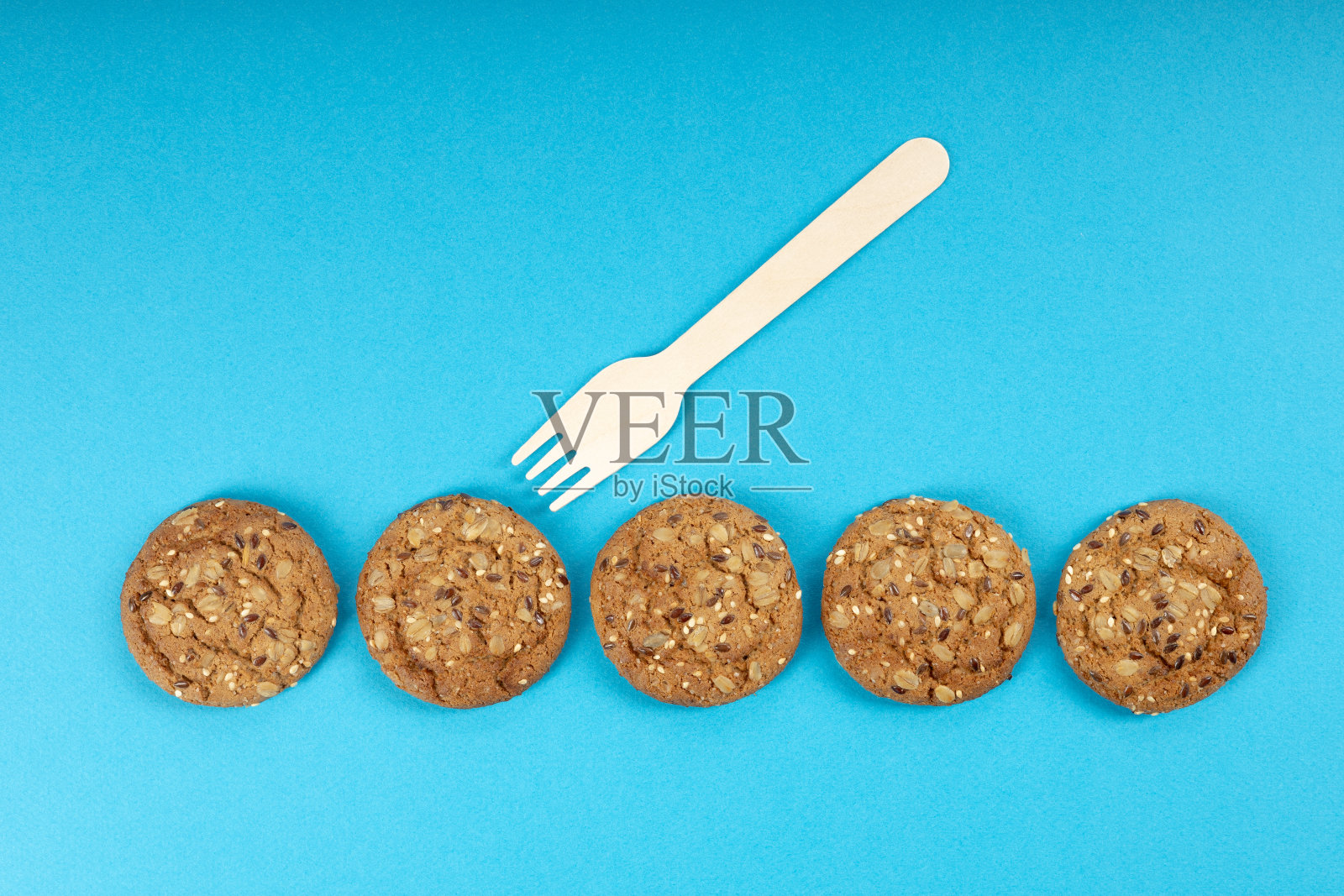 五块燕麦饼干排成一排,在其中一块饼干上放着一把木叉照片摄影图片