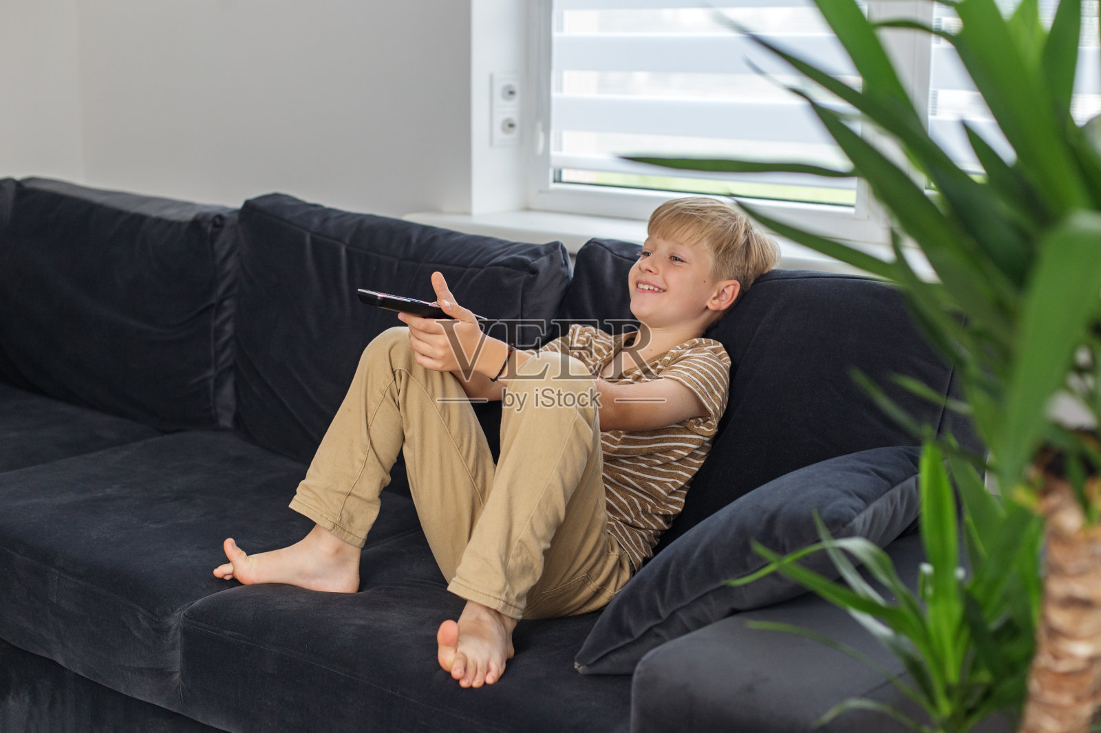 小男孩坐在沙发上看电视和有趣的电影。男孩拿着电视遥控器。放学后休息照片摄影图片