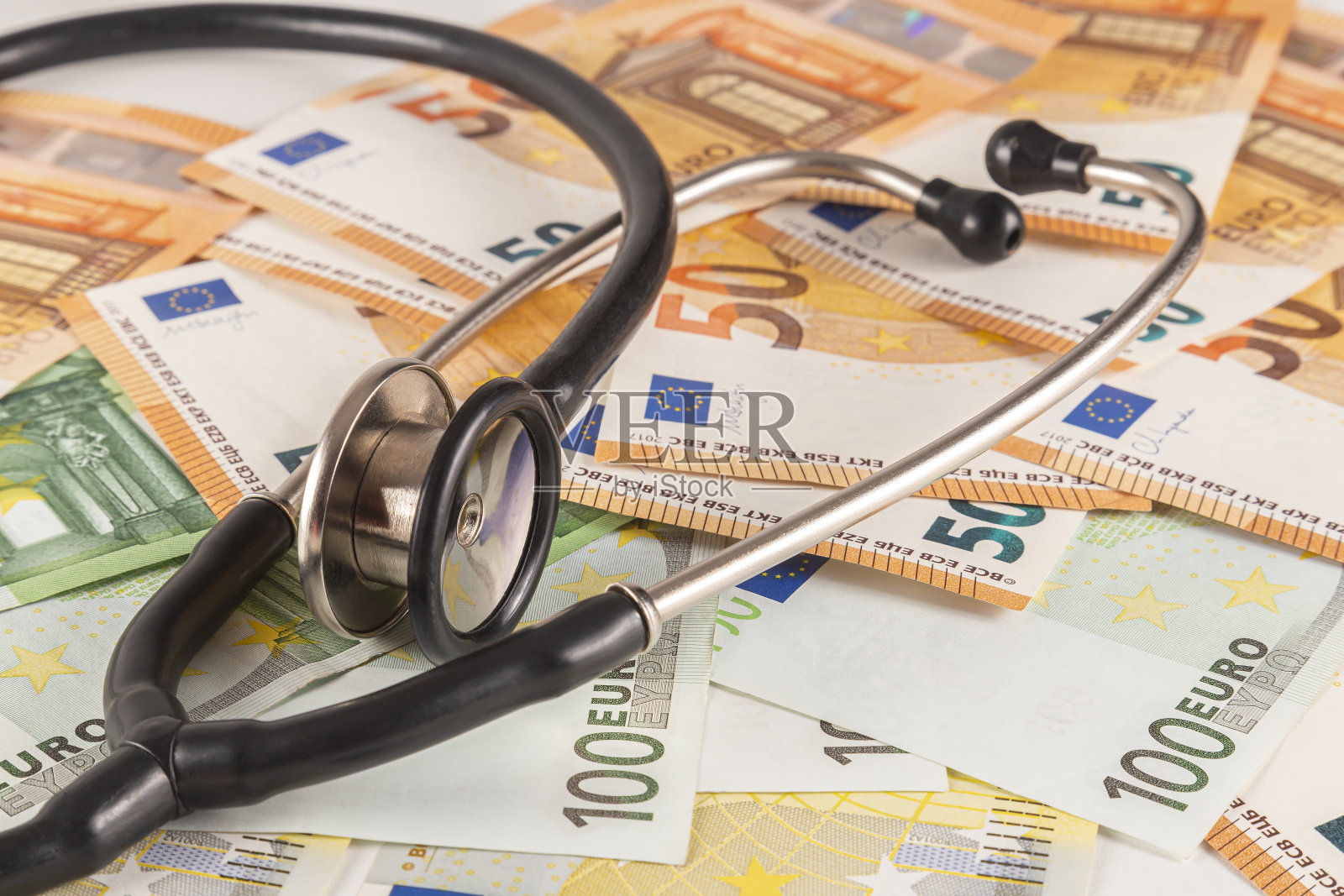 一个听诊器放在一张桌子上,桌子上摆满了欧元纸币,背景是浅色的特写镜头照片摄影图片