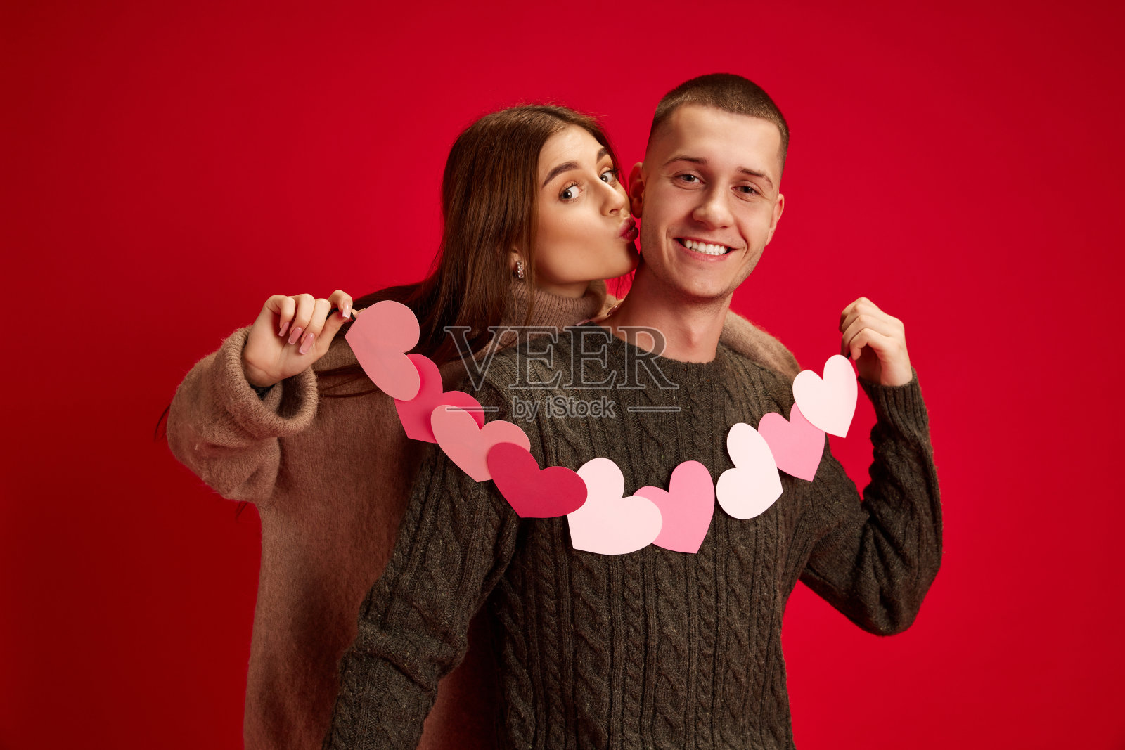 美丽的年轻女人和男人的肖像,幸福的夫妇抱着心,在红色的工作室背景下摆姿势。情人节,恋爱照片摄影图片