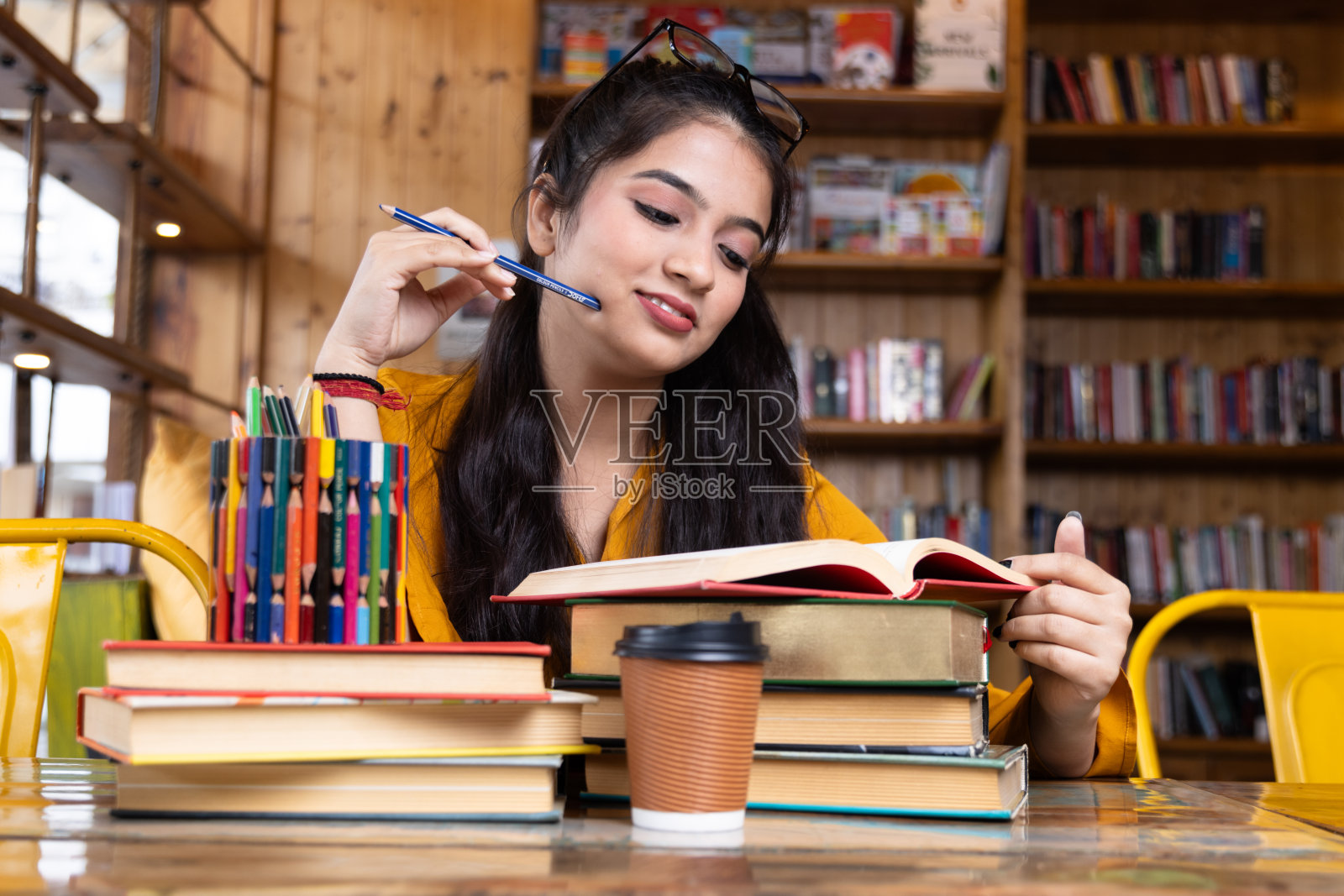 一个漂亮的年轻女孩,商人或学生,戴着眼镜,戴着眼镜,坐在一堆书的座位上,在学校学习,大学图书馆或在公司办公室里,坐在书旁边照片摄影图片