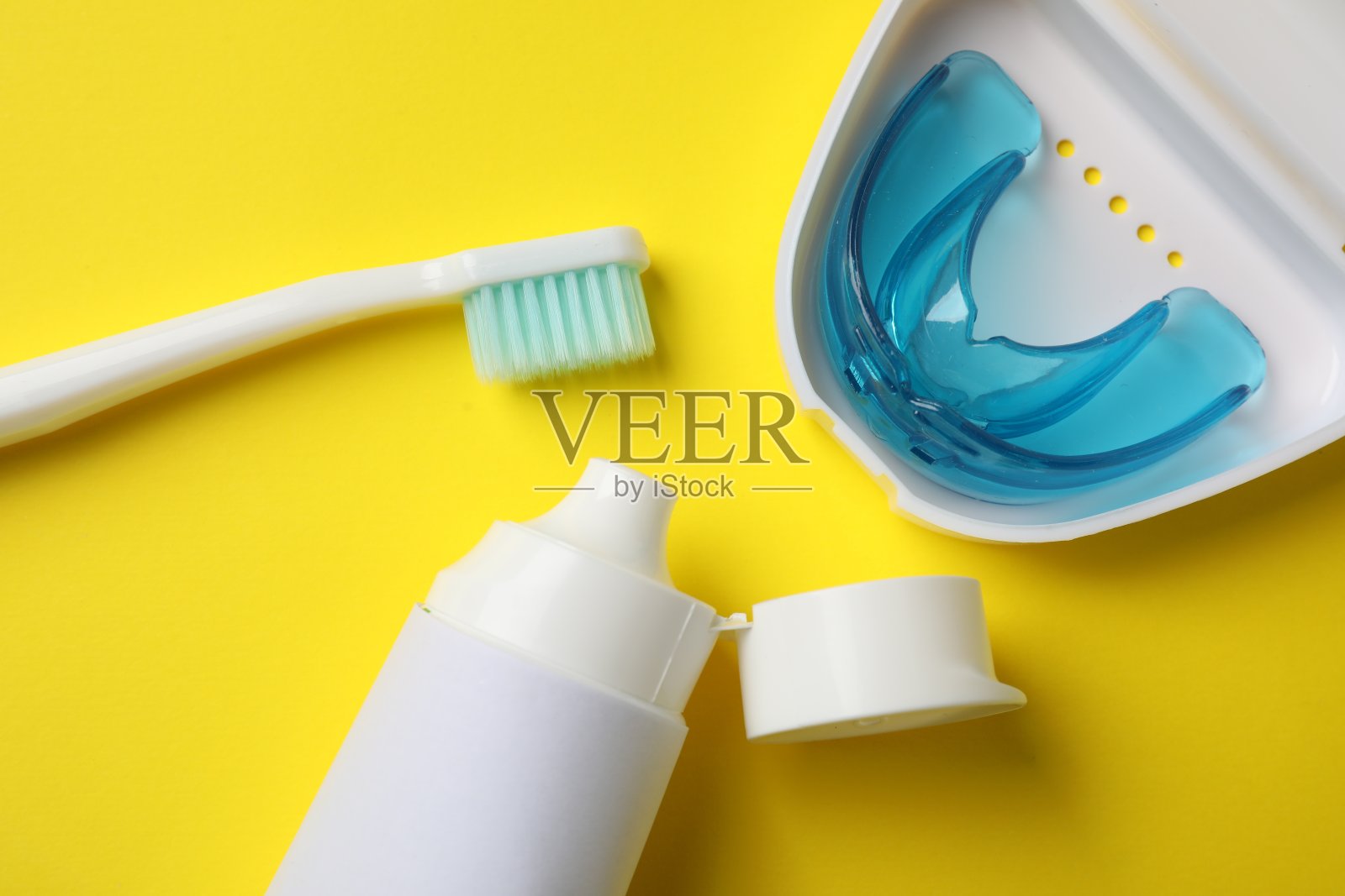 牙膏、牙刷和口腔护套放在黄色底面上,平放。咬校正照片摄影图片