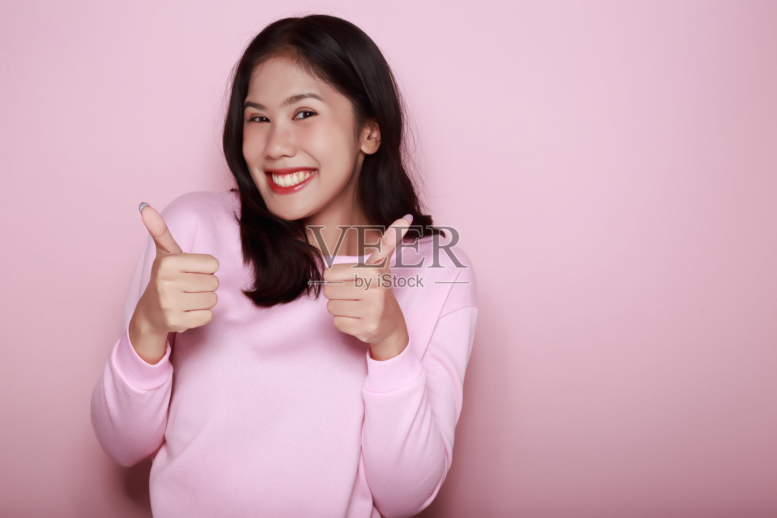 一个漂亮的年轻女子的肖像,在浅粉色的背景下,快乐和微笑,张贴在站立的位置,照片摄影图片